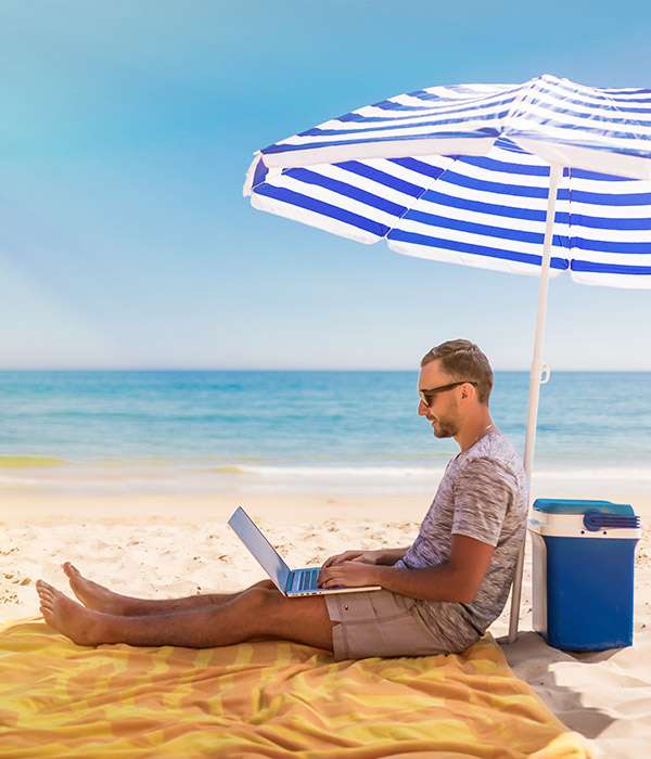 Man on the beach under a sunshade looking at his notebook